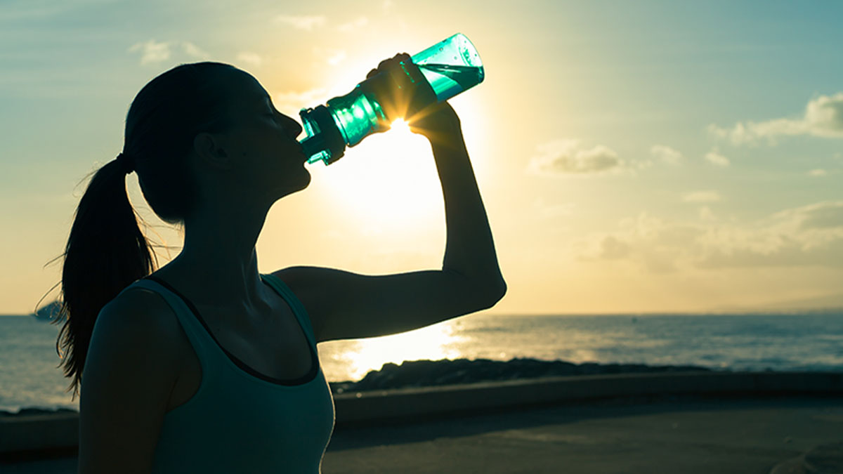 Mulher jovem atleta em contra luz, no exterior a beber água de uma garrafa